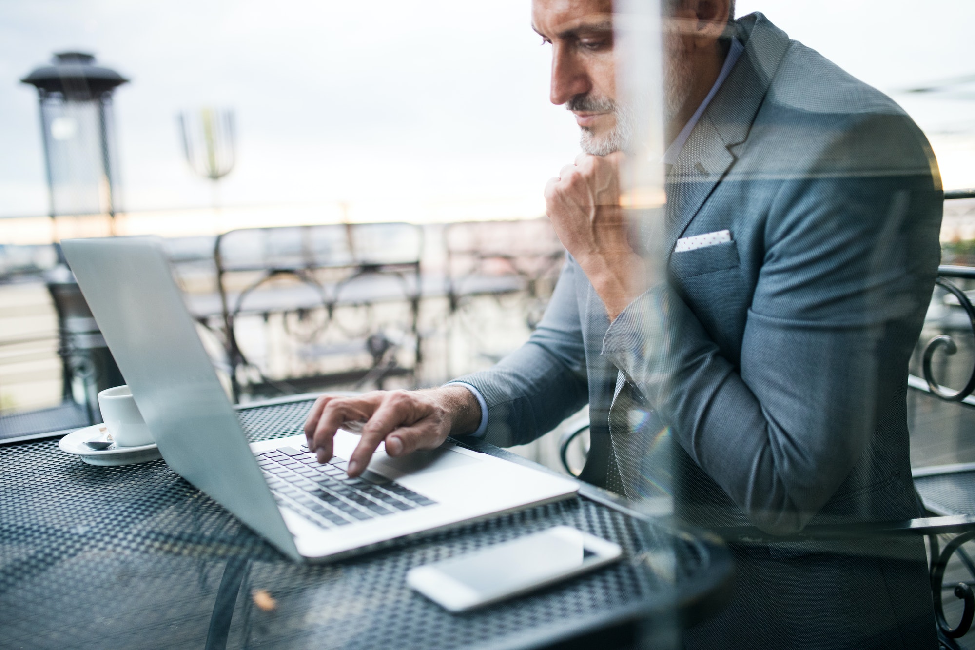 Mature businessman with laptop outside a cafe doing news trading strategy.